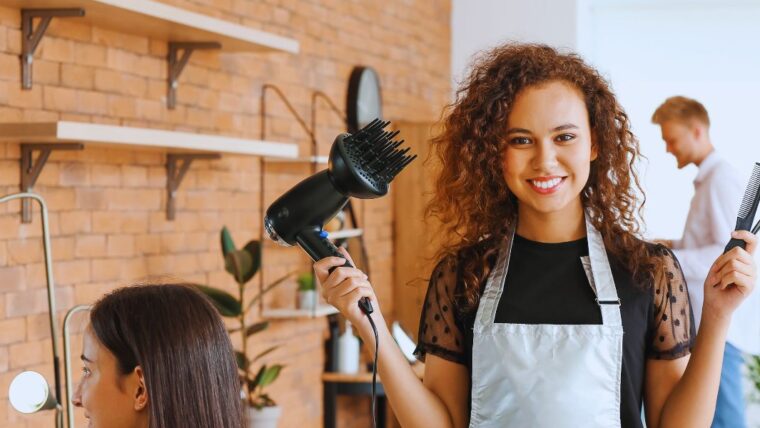 Mains d'un coiffeur tenant une mèche de cheveux mouillés entre deux doigts et la coupant aux ciseaux, peigne fin dans l'autre main