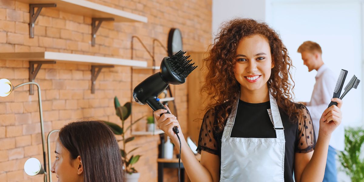 Mains d'un coiffeur tenant une mèche de cheveux mouillés entre deux doigts et la coupant aux ciseaux, peigne fin dans l'autre main