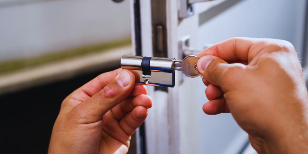 Mains d’un serrurier glissant un cylindre en laiton dans une porte en bois, trousseau de clés posé à côté