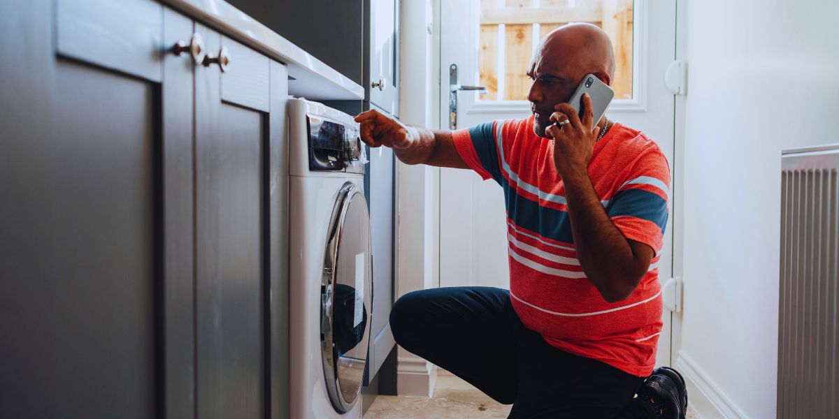 Mains gantées d'un technicien démontant le panneau arrière d'un lave-linge, courroie et tambour visibles sur l'établi