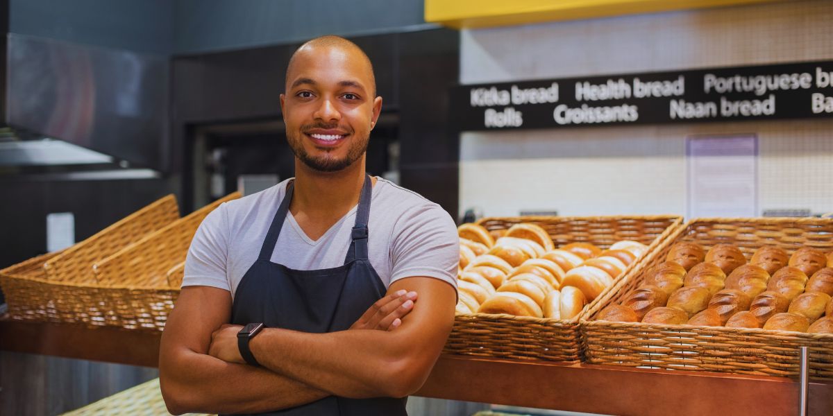 Mains farinées d’un boulanger qui incise à la lame une baguette crue posée sur une plaque, devant la bouche du four