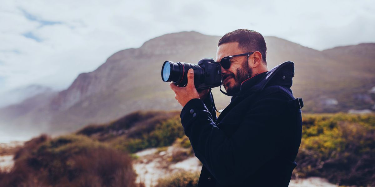 Mains d’un photographe réglant la bague de mise au point d’un boîtier reflex noir, objectif pointé vers un couple à contre-jour