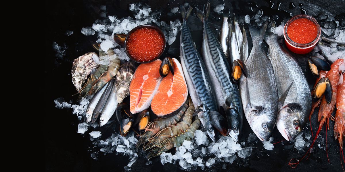 Mains d'un poissonnier levant un filet au couteau sur un poisson entier posé sur de la glace pilée