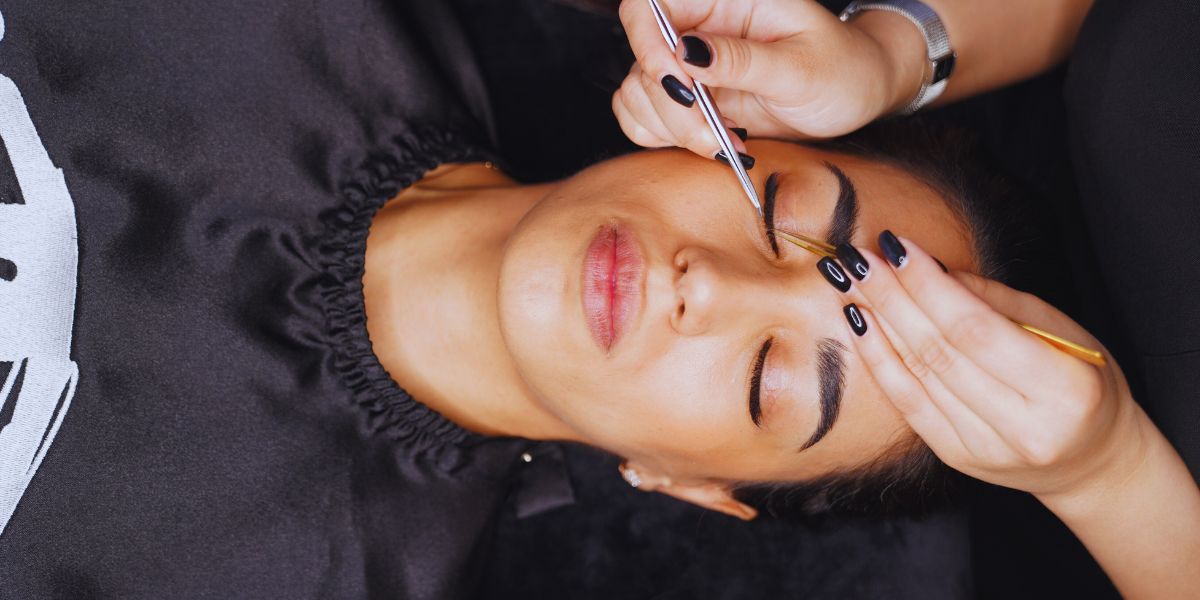 Mains gantées d'une esthéticienne étalant un masque crémeux sur le visage d'une cliente allongée en cabine
